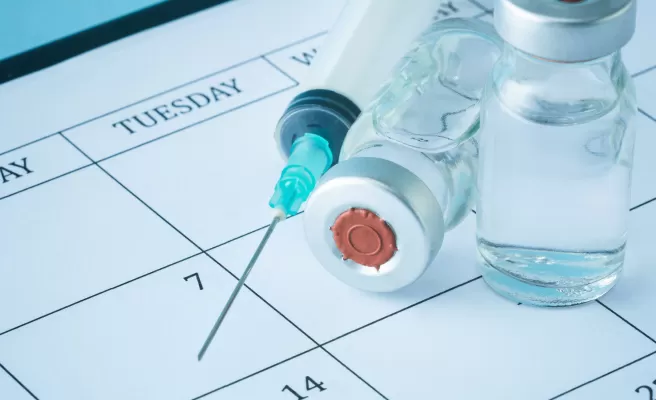 Frascos de vacina e seringa apoiados sobre uma folha de calendário