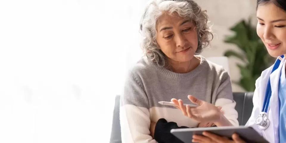 Médica e paciente idosa conversando e olhando para tablet