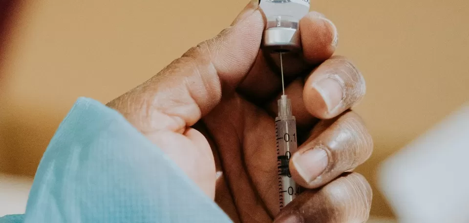Mãos de profissional da saúde segurando ampola e seringa de vacina