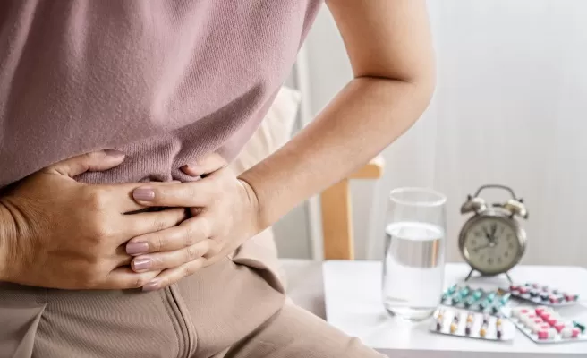 Mulher com as mãos na região gastrointestinal e remédios ao fundo