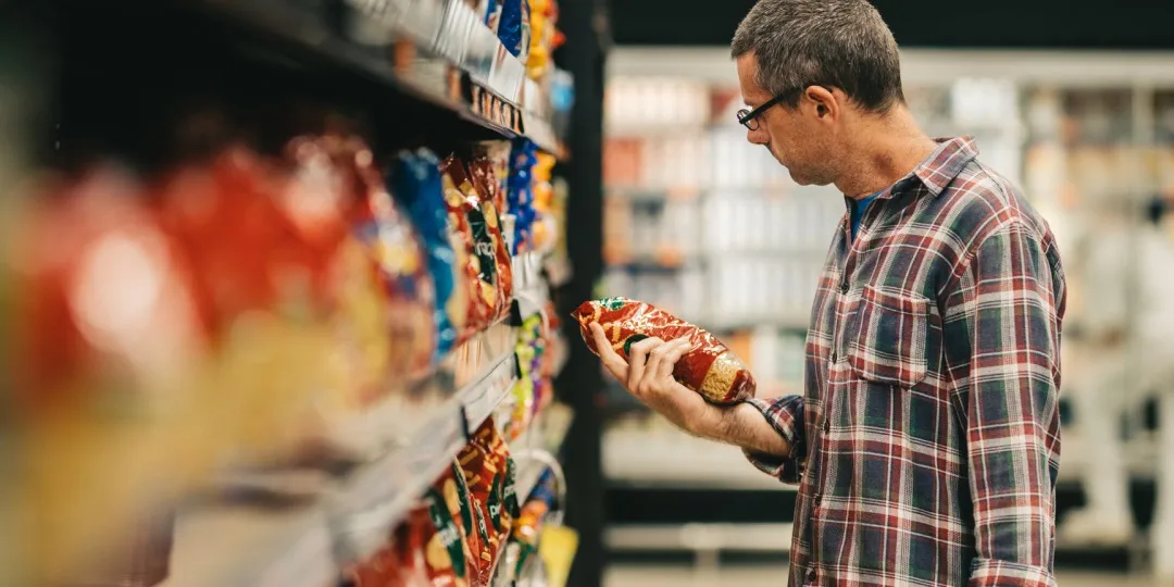 Homem olha embalagem de produto no corredor de supermercado
