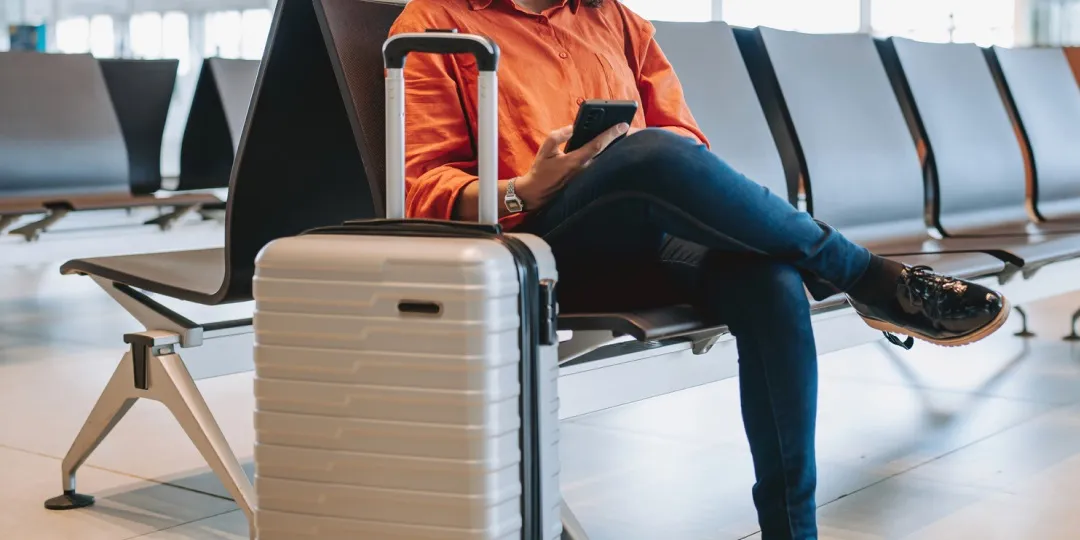 Mulher com mala aguarda sentada no saguão do aeroporto